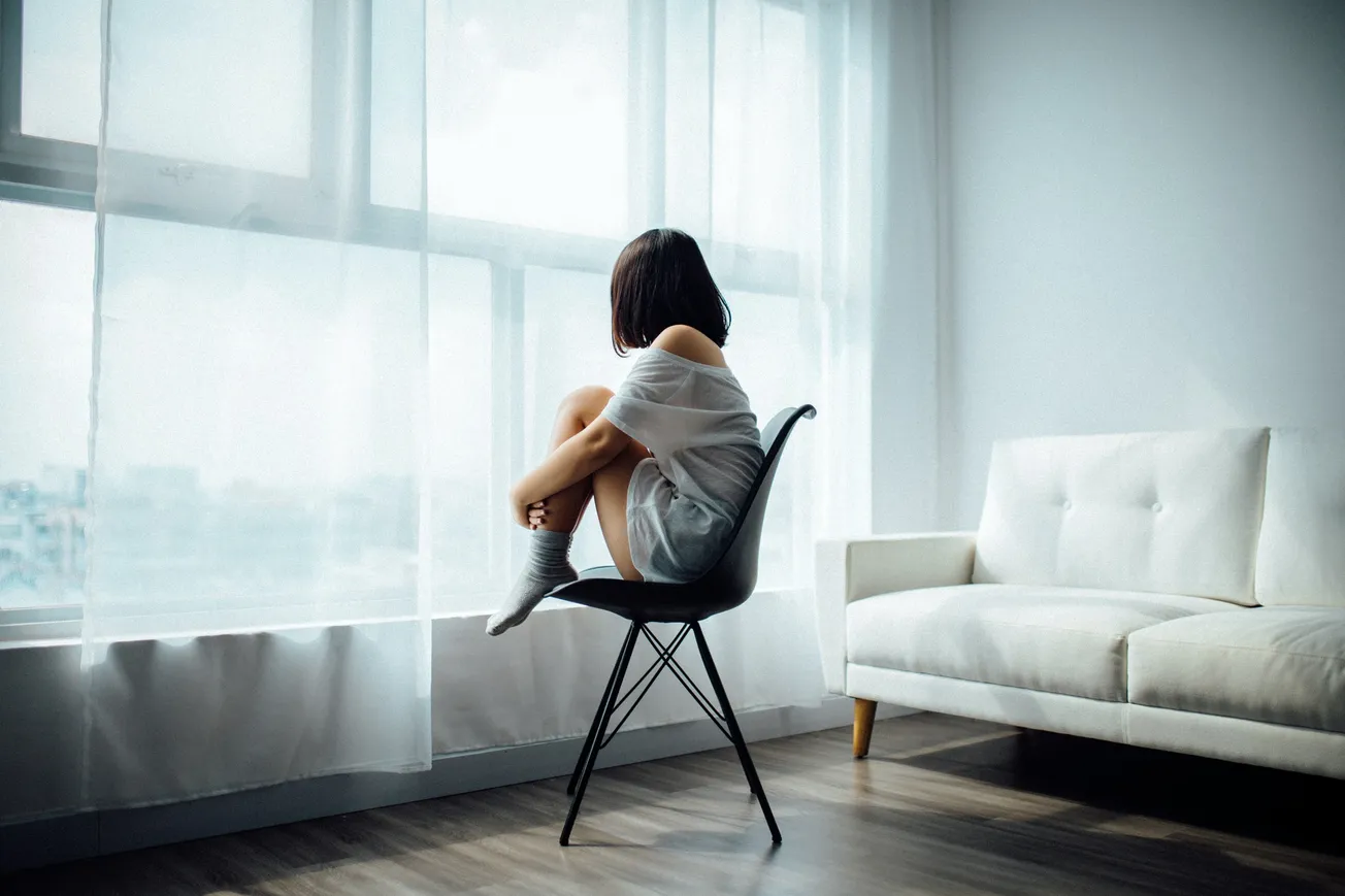 Girl holding legs in chair looking out of window