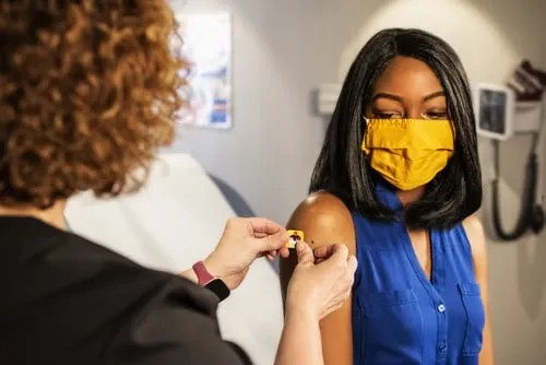 Nurse administering a vaccine to lady with yellow mask