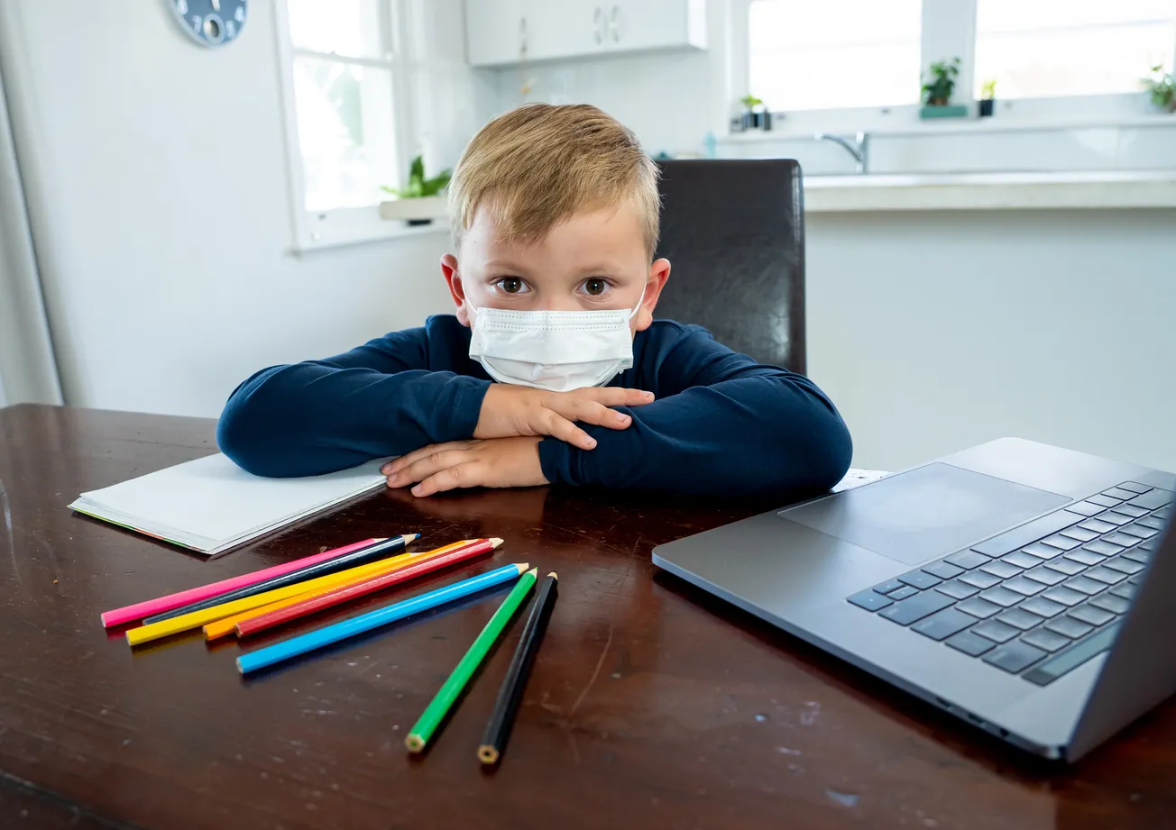Child wearing a mask sitting at a desk doing work